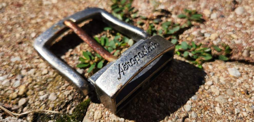 a belt buckle branded Aeropostale in cursive, stylized writing sitting on bricks.