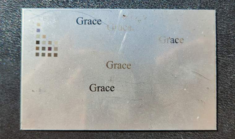 a small, metal placard with the word grace written on it haphazardly in varying tones of grey. there is a color test chart in the top-left corner.